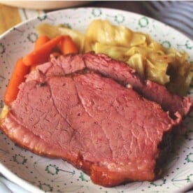 smoked corned beef and cabbage, sliced and served on a white plate with a side of baby carrots