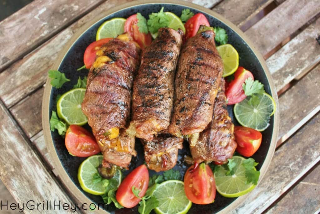 Fajita Steak Roll Ups on a black plate, surrounded by sliced tomatoes and limes.