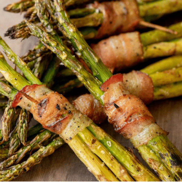 Small bundles of bacon wrapped asparagus stacked on a wooden board.