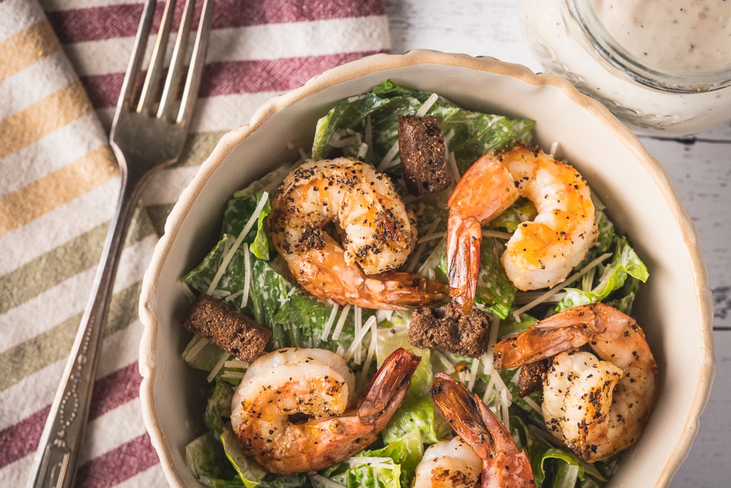 Lemon pepper grilled shrimp on top of a bed of lettuce in a round bowl.