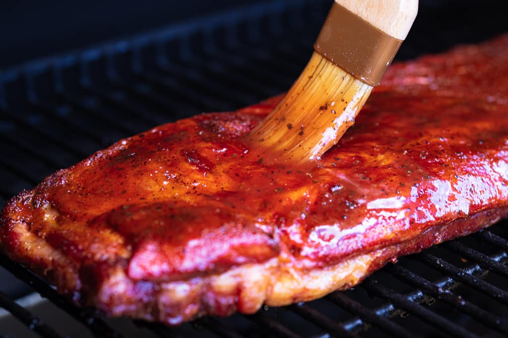 BBQ sauce being basted on a rack of hot and fast ribs.