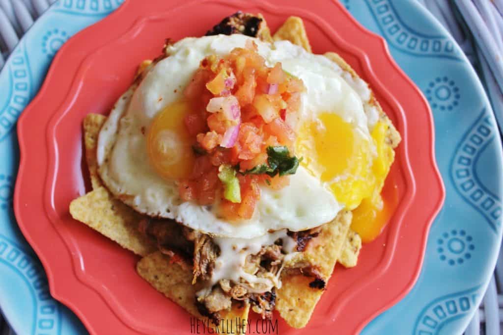 Blue plate with a pile of tortilla chips topped with pulled pork, cheese, eggs, and fresh salsa.