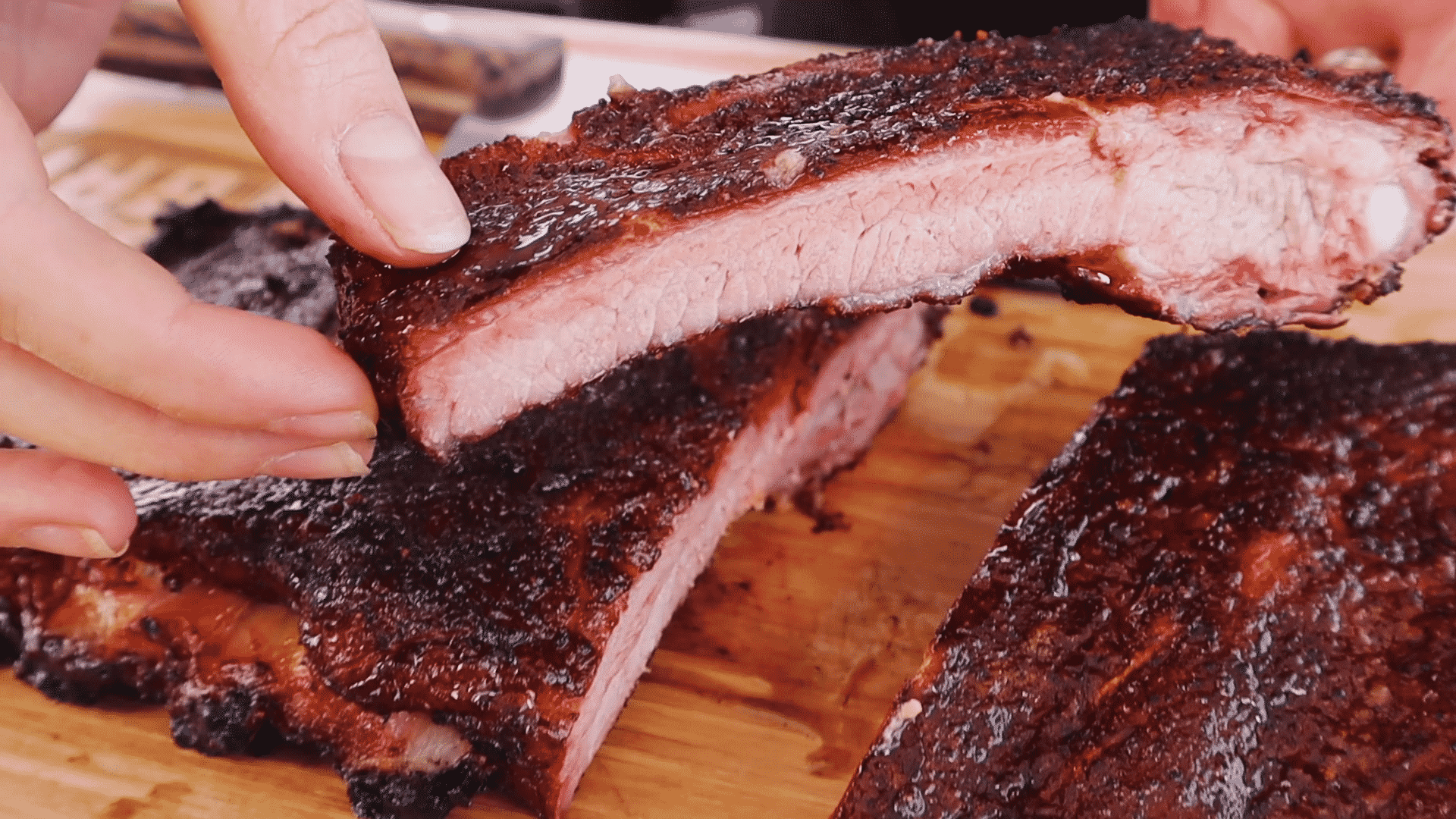 One low and slow rib held above a rack of low and slow ribs.