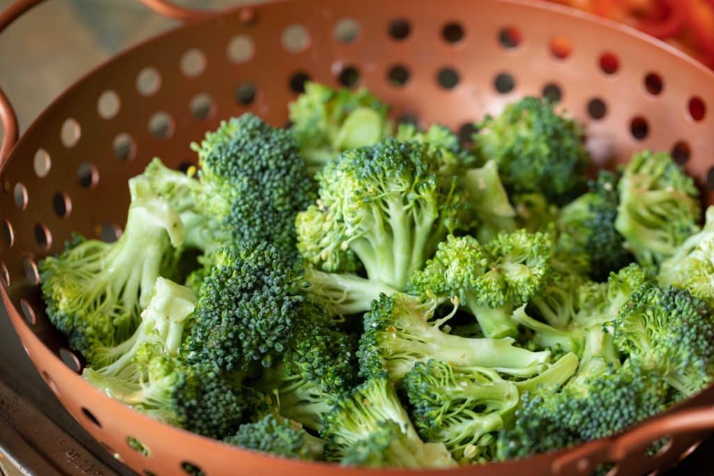 Raw broccoli florets in a copper vegetable basket.