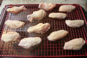Uncooked chicken wings arranged on a red wire rack atop a metal baking sheet