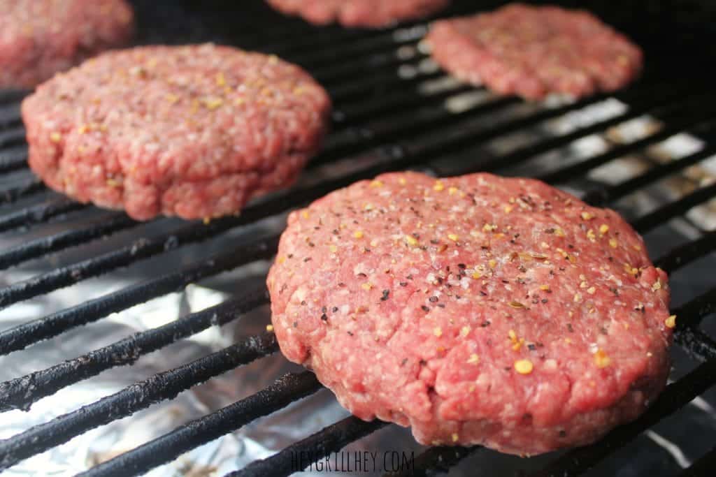 Uncooked hamburger patties on the grill grate.