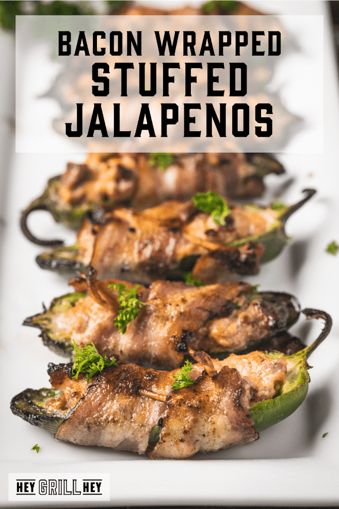 Grilled stuffed jalapenos lined up on a serving platter with text overlay - Bacon Wrapped Stuffed Jalapenos.