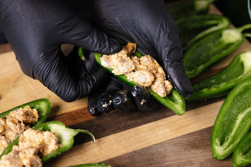 Bratwurst and cream cheese filling being stuffed in a jalapeno half.
