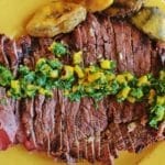 Overhead view of sliced London broil on a yellow plate. Meat is topped with cilantro gremolata.