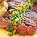Sliced London broil on a yellow plate and topped with cilantro gremolata.