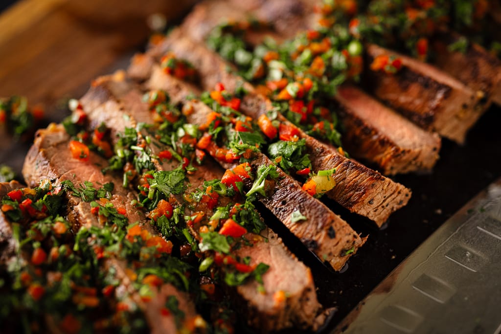 Sliced London broil on a wooden cutting board topped with cilantro gremolata.