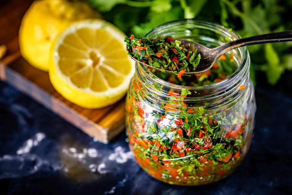 Cilantro gremolata in a small glass mason jar with sliced lemons in the baground.