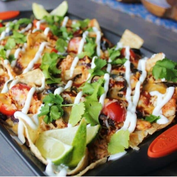 BBQ chicken nachos topped with cheese, black olives, tomatoes, sour cream, and cilantro on a rimmed baking sheet