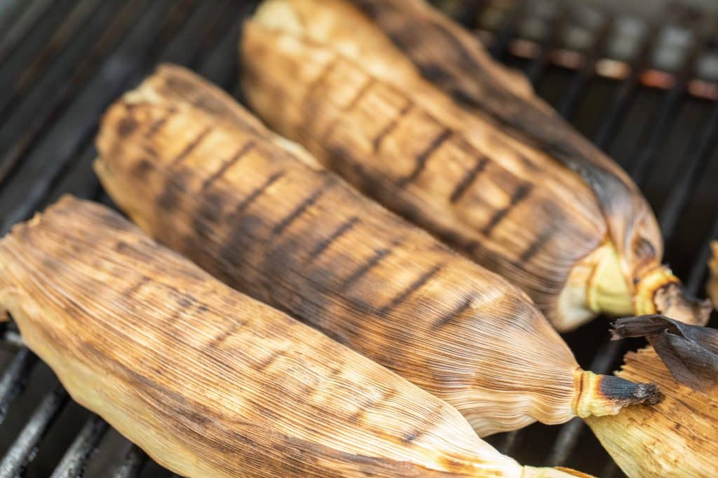 3 corn on the cob in husks on the grill
