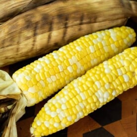 Two corn on the cob on a wood cutting board
