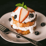 Grilled lemon cake topped with whipped cream and fresh blueberries and strawberries on a white plate.