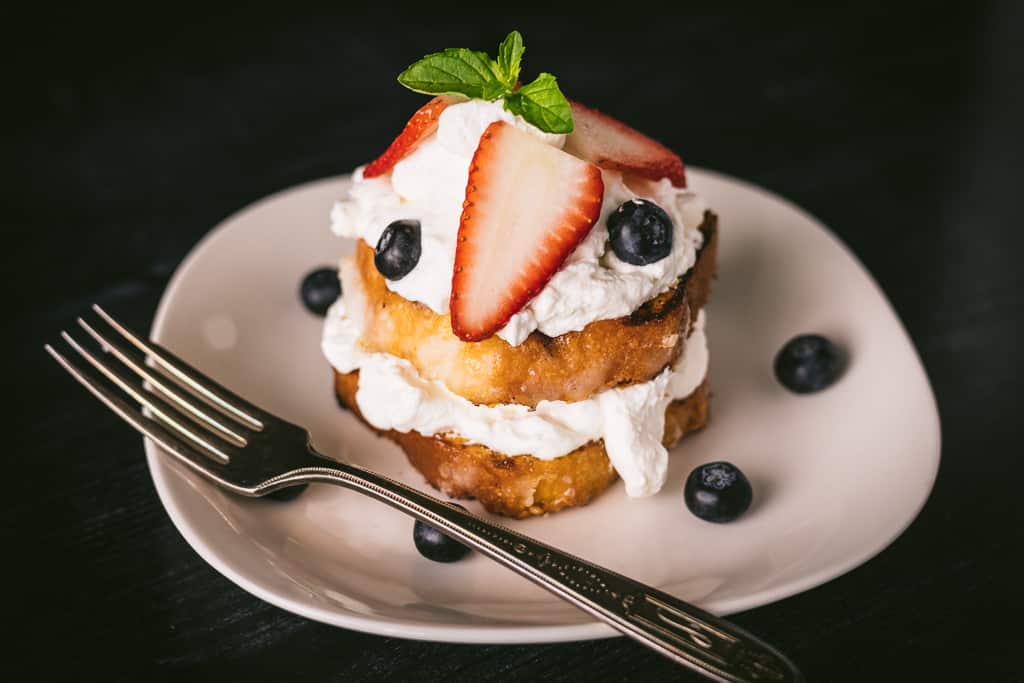Grilled lemon cake topped with whipped cream and fresh blueberries and strawberries on a white plate.
