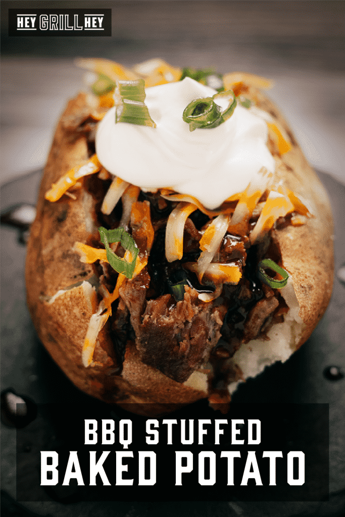 Brisket stuffed baked potato topped with shredded cheese and sour cream with text overly - BBQ Stuffed Baked Potato