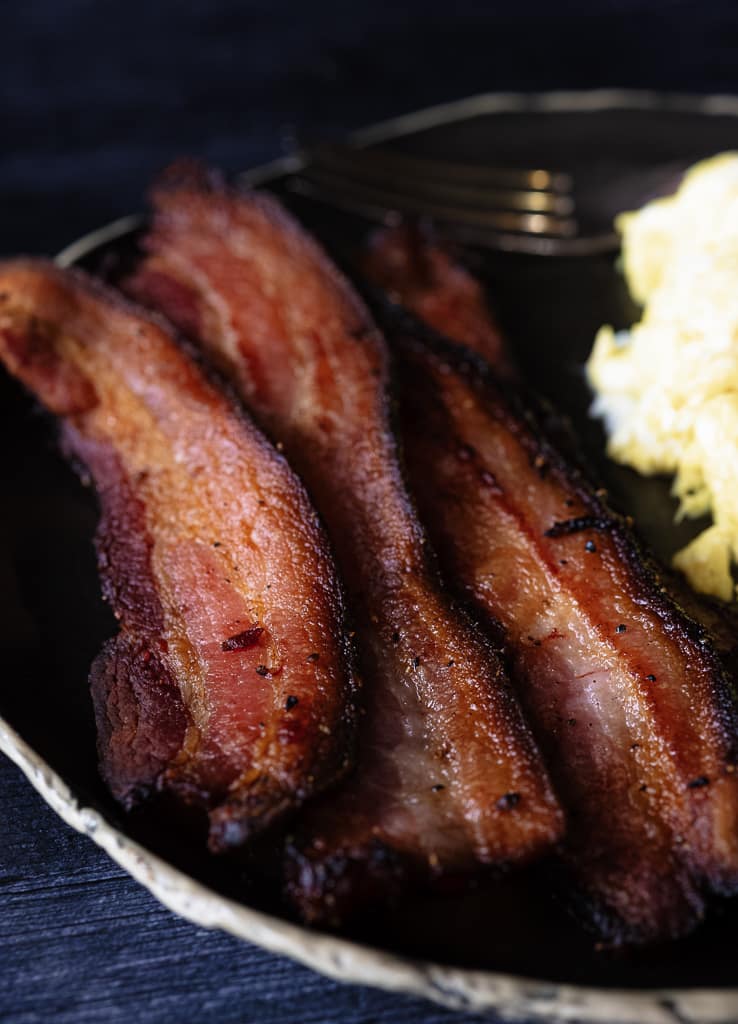 Sliced bacon on a plate next to mashed potatoes.