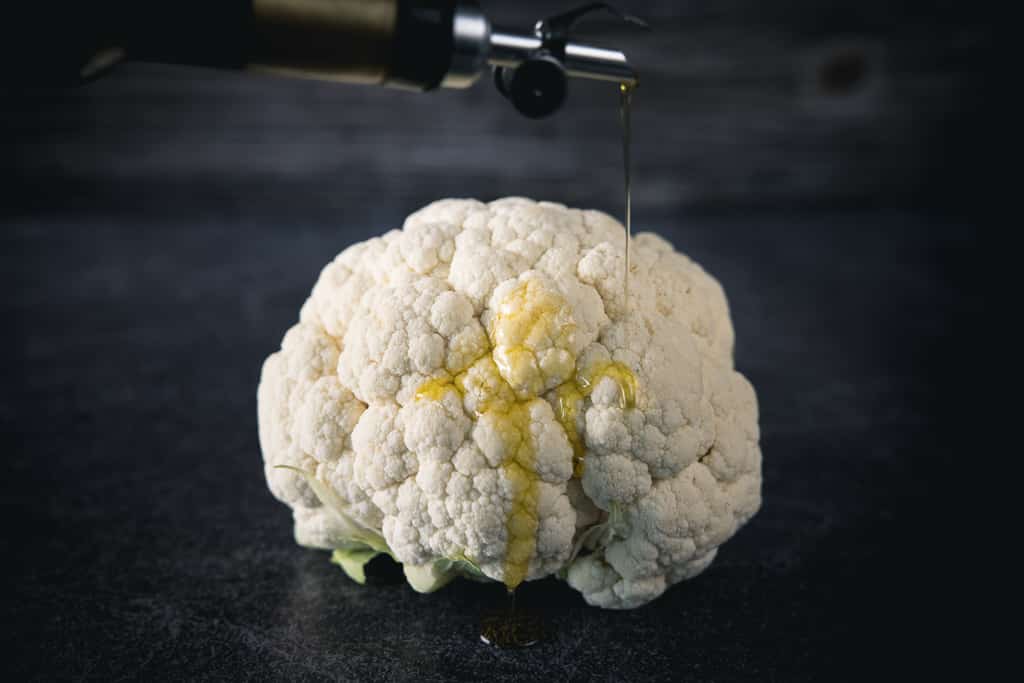 Olive oil being drizzled on a whole head of cauliflower.