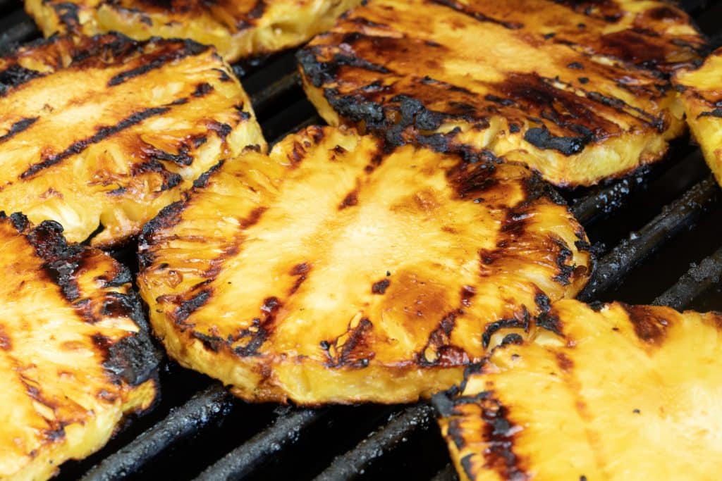 Grilled pineapple with dark grill marks on grill grates.