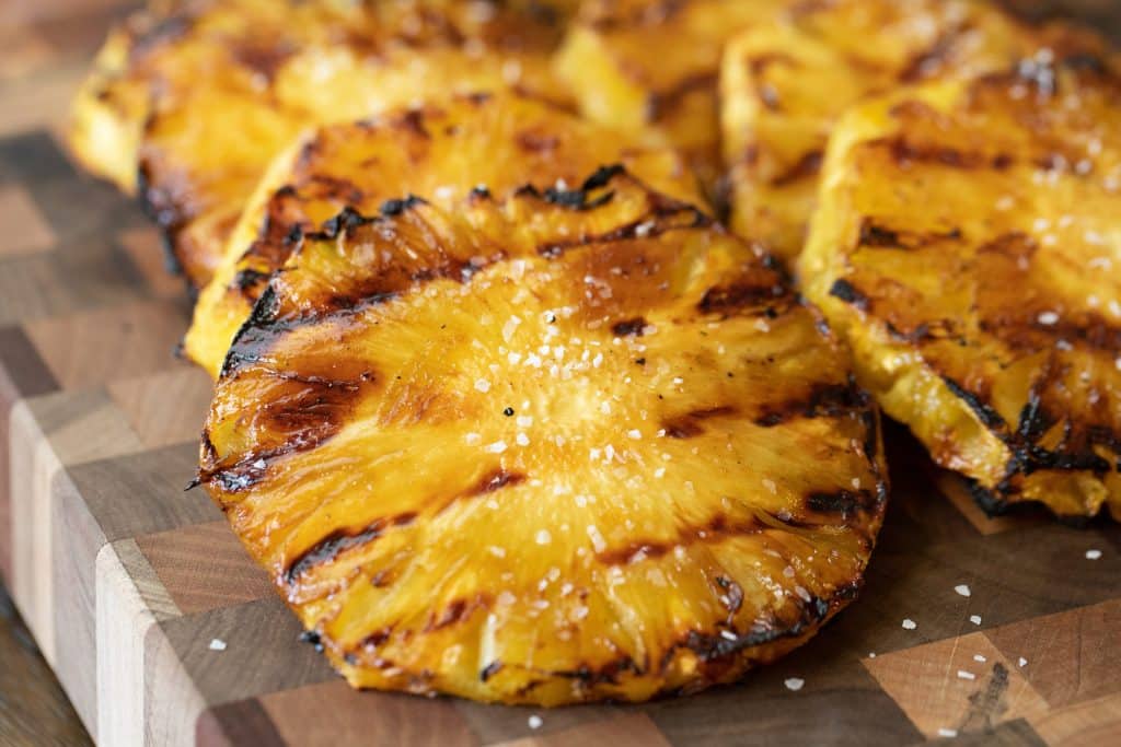 Grilled pineapple with grill marks on a wood cutting board.