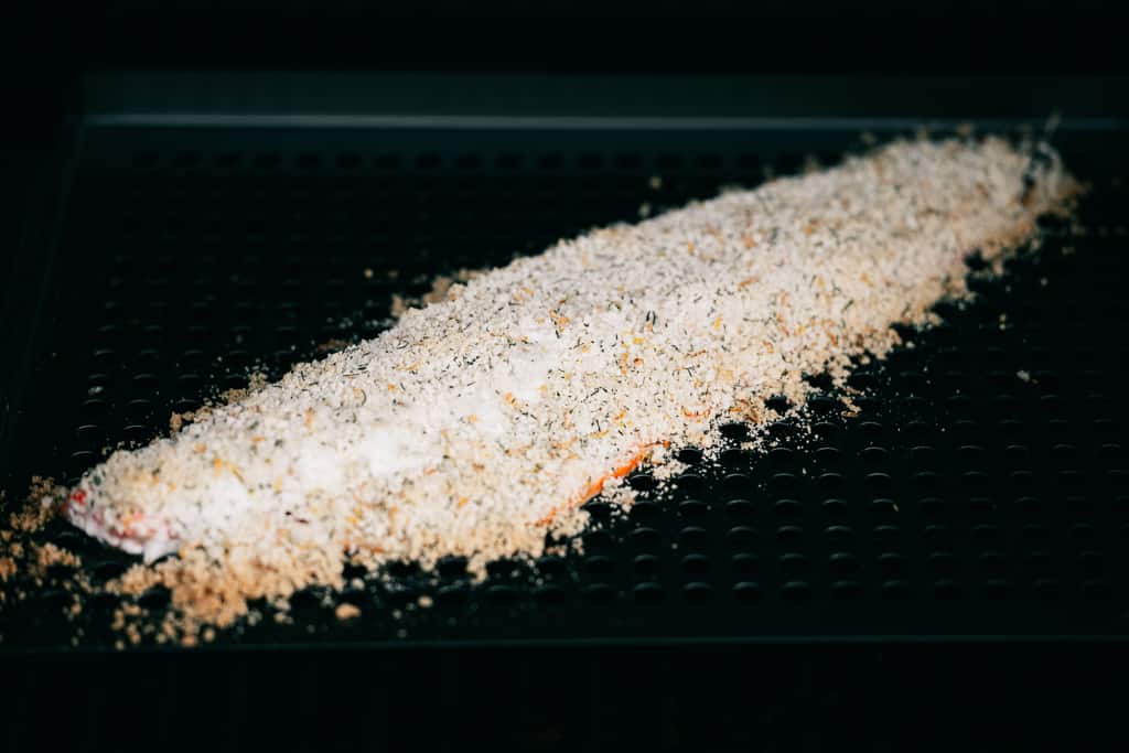 Parmesan sprinkled on the top of a salmon fillet on a grill.