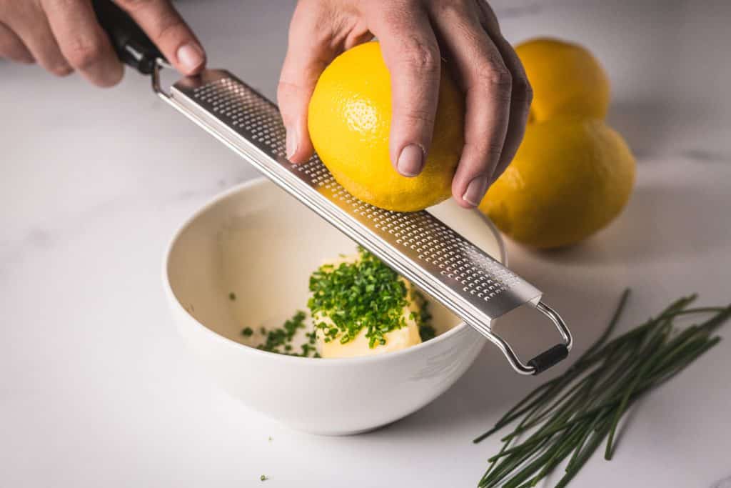 Lemon being zested into a bowl of butter and chives.