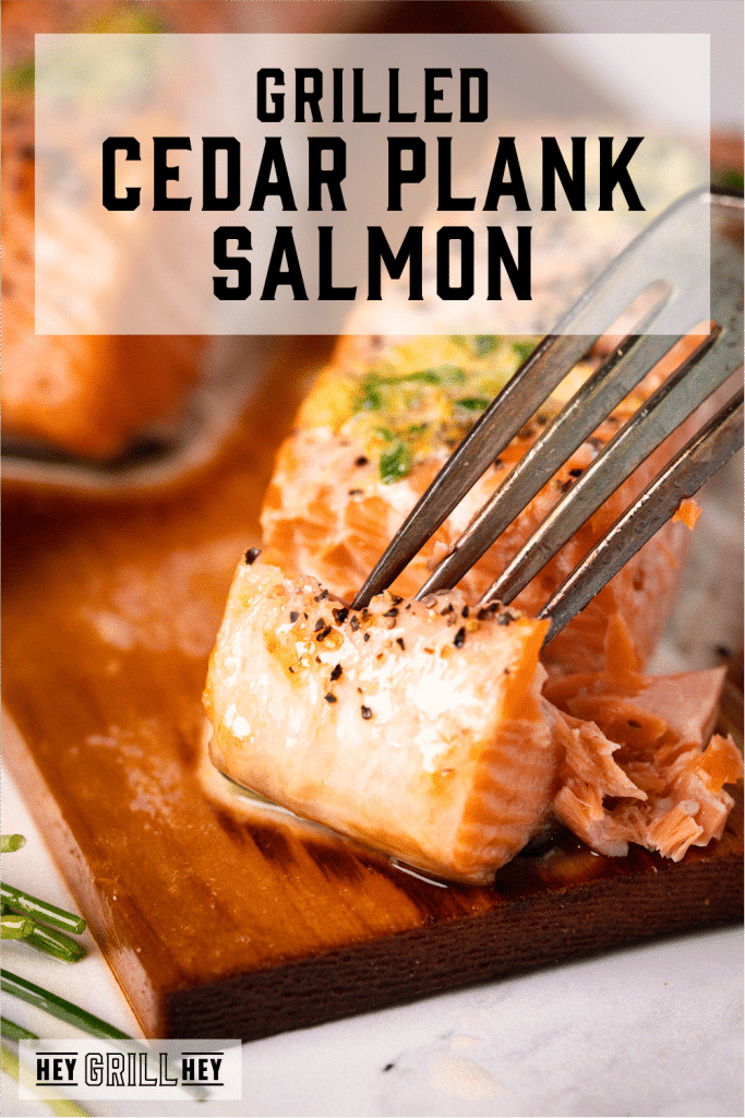 Fork flaking into a grilled salmon filet on a cedar plank with text overlay- Grilled Cedar Plank Salmon.
