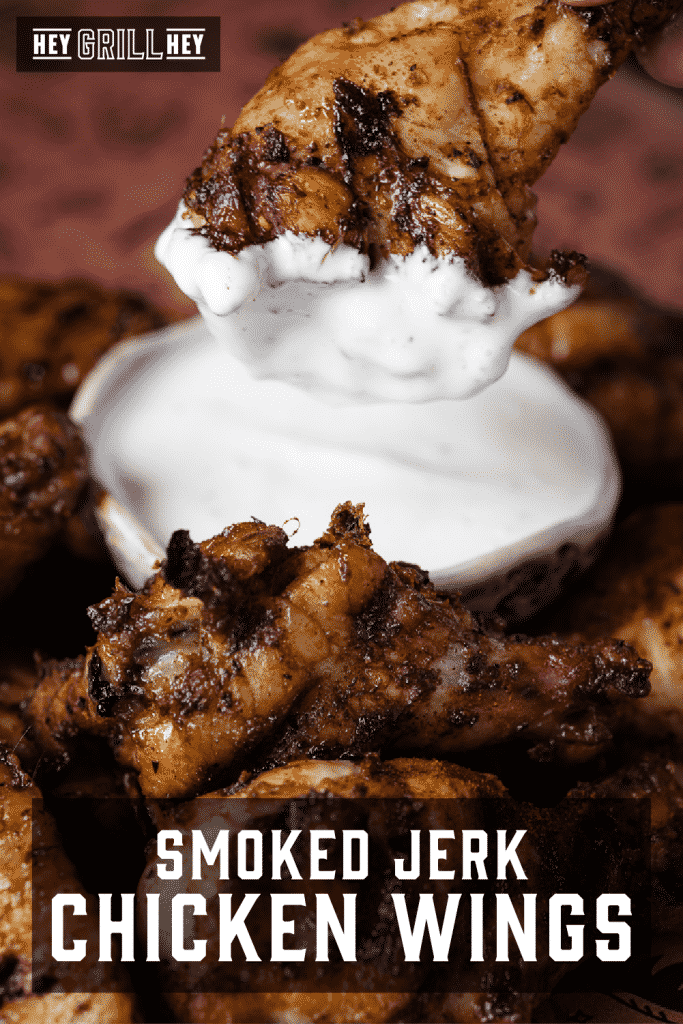 Smoked jerk chicken wing dipped in ranch surrounded by a pile of chicken wings.