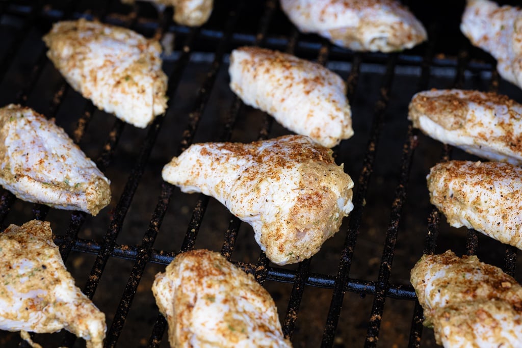 Marinated chicken wings on grill grates of a smoker.