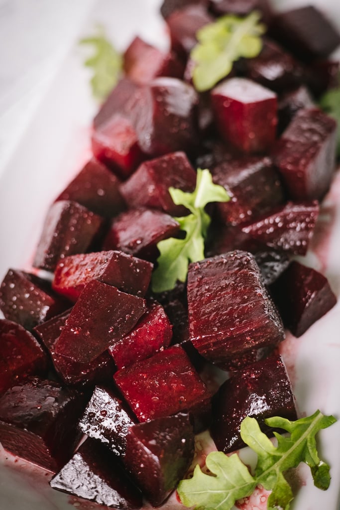 Grilled beets on a white plate garnished with fresh greens.