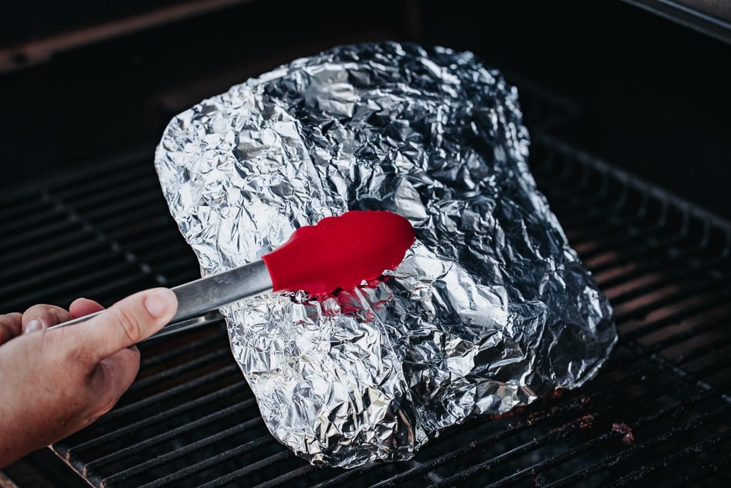Beets in an aluminum foil pouch being rotated on a grill.