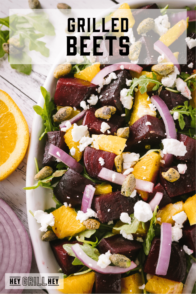 Grilled beets, sliced onions, fresh oranges, feta cheese, pistacios, and greens in a bowl with text overlay - Grilled Beets.