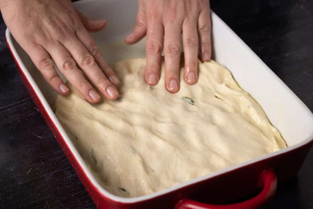 Focaccia bread dough being pressed into a baking dish.