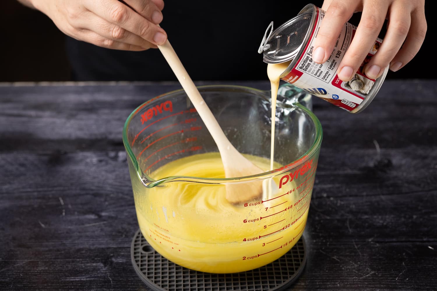 Sweetened condensed milk being poured into a glass measuring cup full of melted butter.