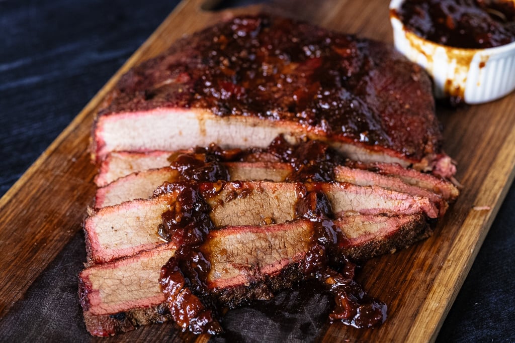 Sliced brisket on a cutting board drizzled with bacon BBQ sauce.