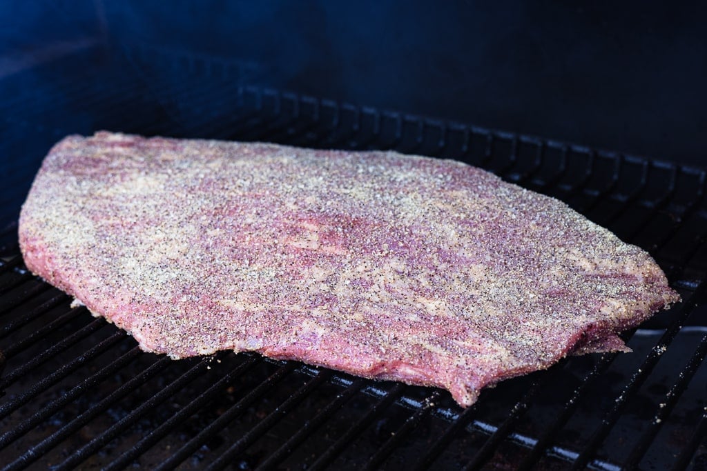 Seasoned brisket on the grill grates of a smoker.