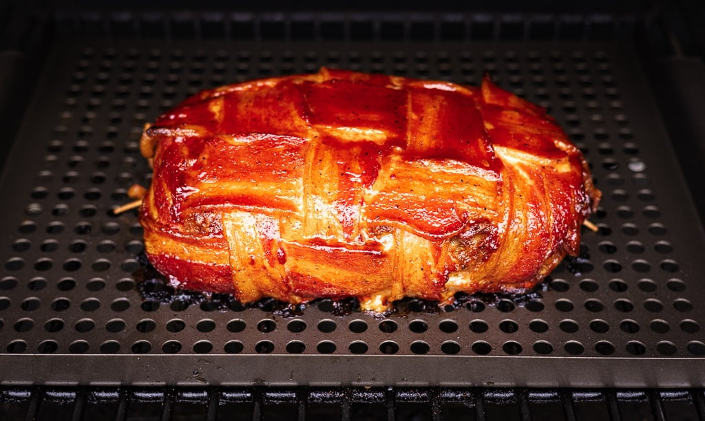 Bacon wrapped BBQ meatloaf on the grill grates of a pellet smoker.