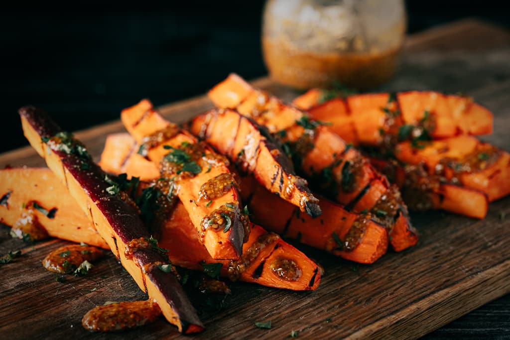 Grilled sweet potato fries drizzled with honey mustard on a wooden cutting board.