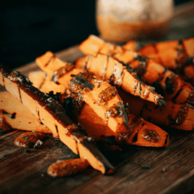 Grilled sweet potato fries drizzled with honey mustard sauce on a wooden cutting board.