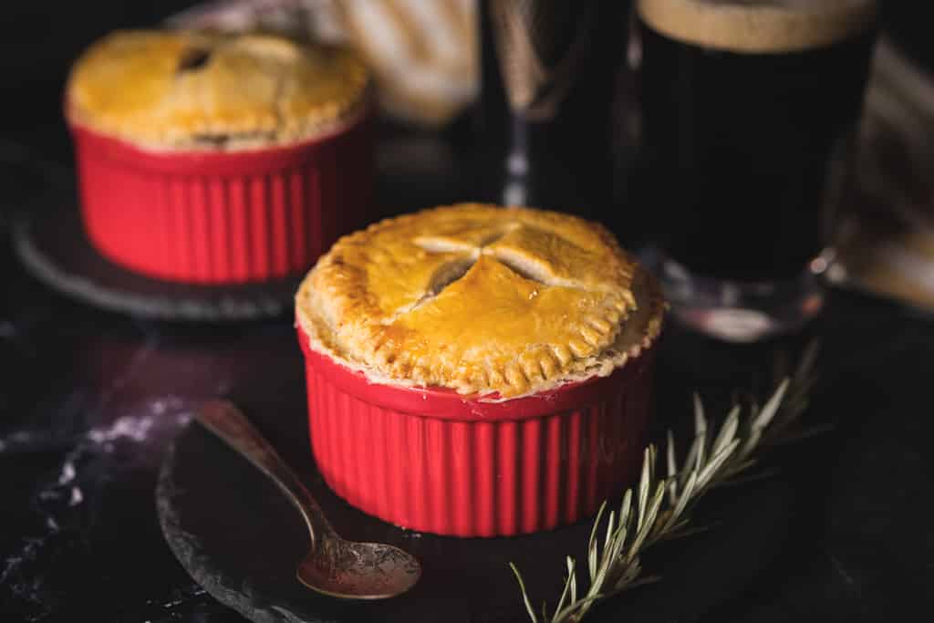 Two Guinness and beef pot pies on a dark marble surface.