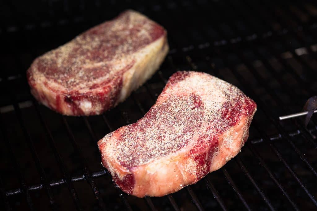 Seasoned rib eye steaks on the grill.