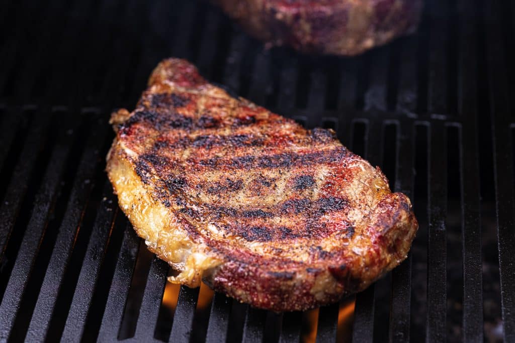 Rib eye steaks with crisscrossed grill marks on a grill.