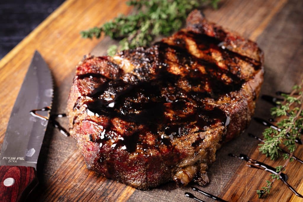 Rib eye steak drizzled with balsamic vinegar on a wooden cutting board.