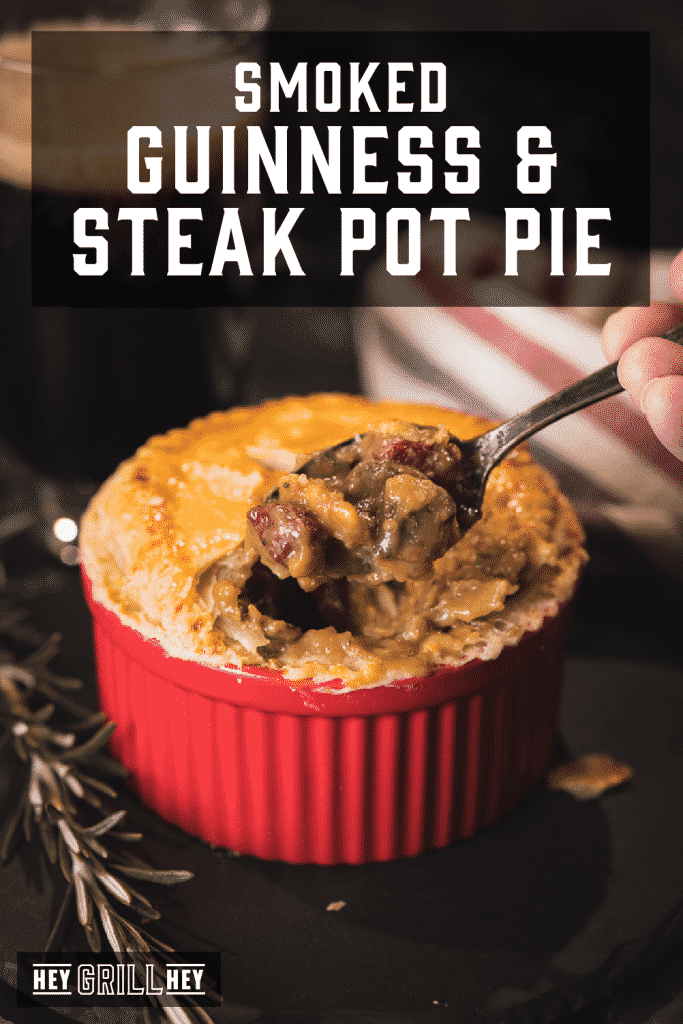 Metal spoon taking a scoop out of a red ramekin filled with beef pot pie. Text overlay reads: Smoked Guinness & Steak Pot Pie.