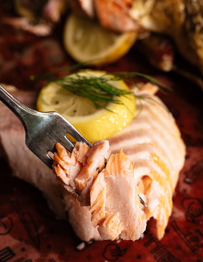 Flaked grilled salmon on a fork with a whole grilled salmon in the background.