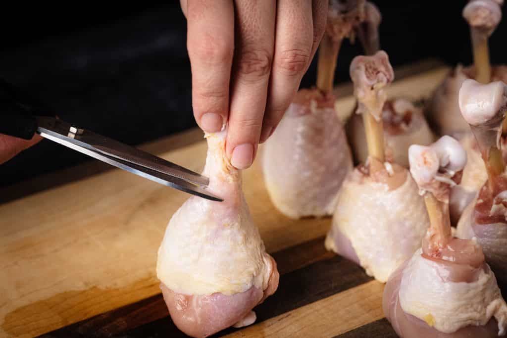 Scissors cutting into the fat on a chicken drumstick.