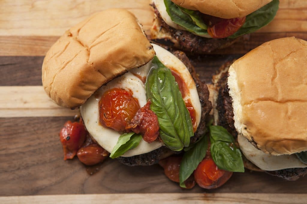 Overhead view of garlic butter burger topped with mozzarella, tomatoes, and basil.