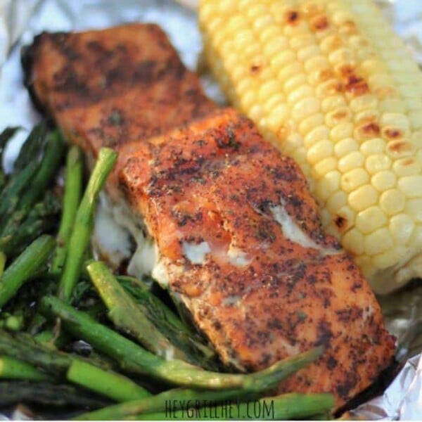 Grilled asparagus, seasoned whole salmon, and an ear of corn on a sheet of aluminum foil.